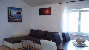 Un salon moderne avec un canapé d’angle, une table à manger avec des chaises, une petite table en verre et deux tableaux accrochés au mur.