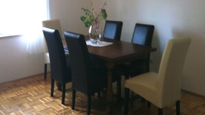 Un coin repas avec une table en bois, quatre chaises, un vase de fleurs et un tableau représentant un coucher de soleil accroché au mur.