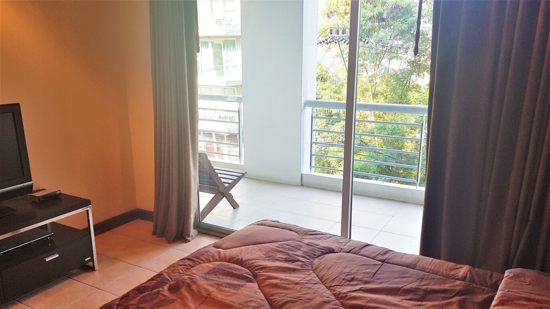 Hotelkamer met een bed, een televisie, een balkon met stoel en uitzicht op groen.