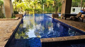 A swimming pool with clear blue tiles, surrounded by stone steps and palm trees.