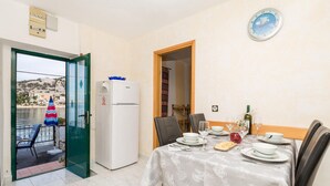 Un coin repas avec une table dressée pour deux personnes, un réfrigérateur et une vue sur une étendue d’eau, visible à travers une porte ouverte.