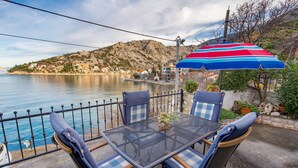 Une terrasse en bord de mer avec une table et des chaises, un parasol à rayures et une vue sur une ville côtière.