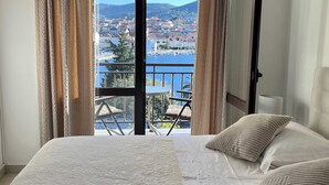 A bedroom with a bed, curtains, and a view of a town and sea.