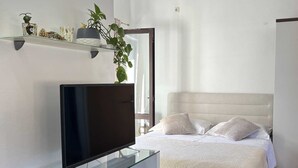 A modern bedroom with a bed, a TV on a glass shelf, and a plant on a shelf.