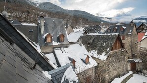 Un edificio de piedra tradicional con varios tejados a dos aguas y ventanas de madera, rodeado de montañas nevadas.