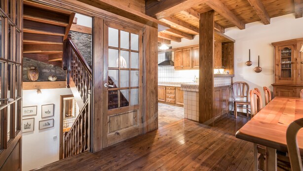 Un interior de madera con una escalera que lleva al segundo piso, un comedor con mesa de madera y armarios de cocina.
