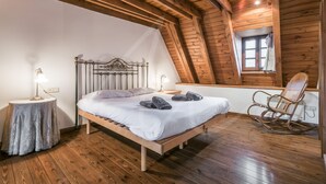 Una habitación con estructura de madera, una cama, dos mesitas de noche, un sillón mecedor y un ventanal.