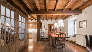 Un comedor amplio con suelo de madera y un techo alto. Hay una mesa de madera rodeada de sillas.