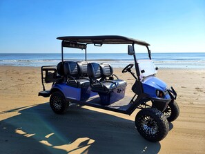 A golf cart parked on a sandy beach with the ocean in the background.
