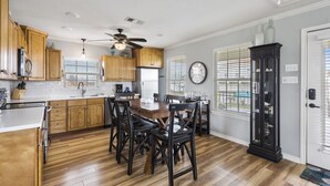 A kitchen with wooden cabinets, a dining table with chairs, a ceiling fan, and a clock on the wall.