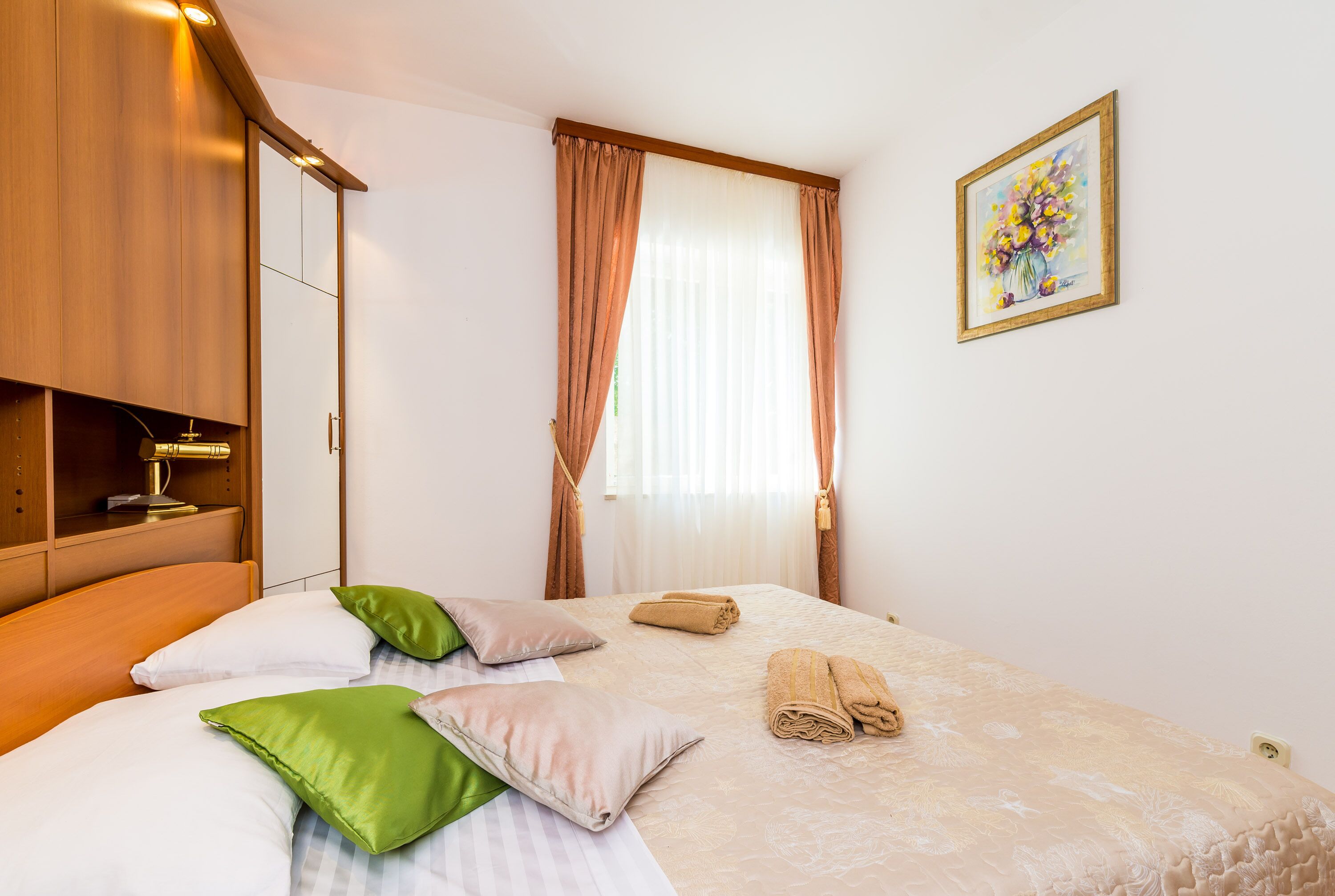 A hotel room with a bed, pillows, a wardrobe, a painting, and a window with curtains.
