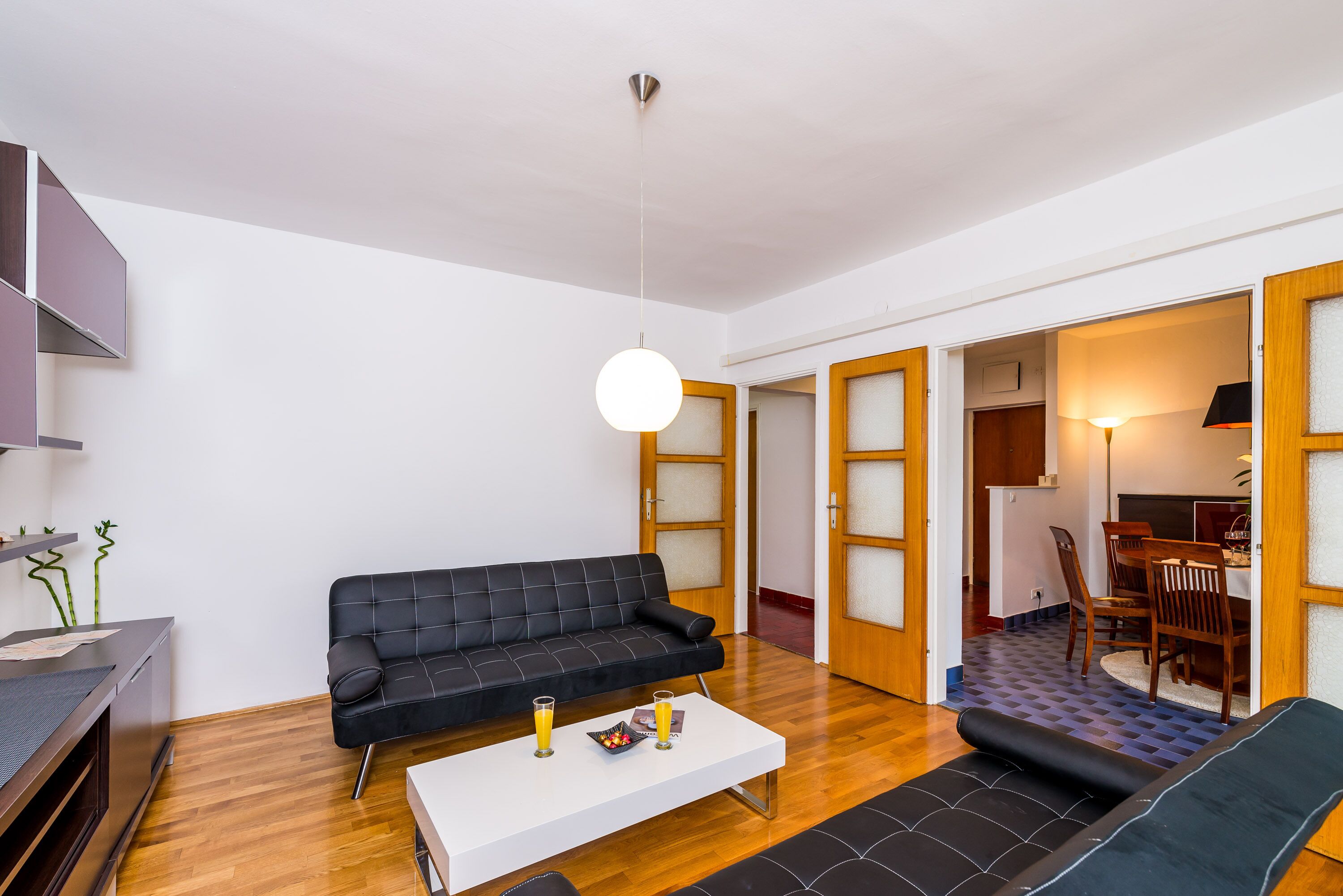 Ein modernes Wohnzimmer mit einem schwarzen Sofa, einem weißen Couchtisch und einem Essbereich mit Holzsesseln und einem Tisch.