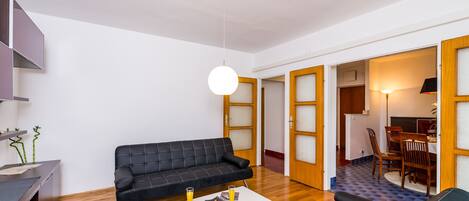 Ein modernes Wohnzimmer mit einem schwarzen Sofa, einem weißen Couchtisch und einem Essbereich mit Holzsesseln und einem Tisch.