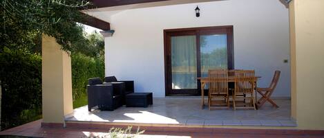A covered patio area with a table and chairs, a sliding glass door, and a small garden.
