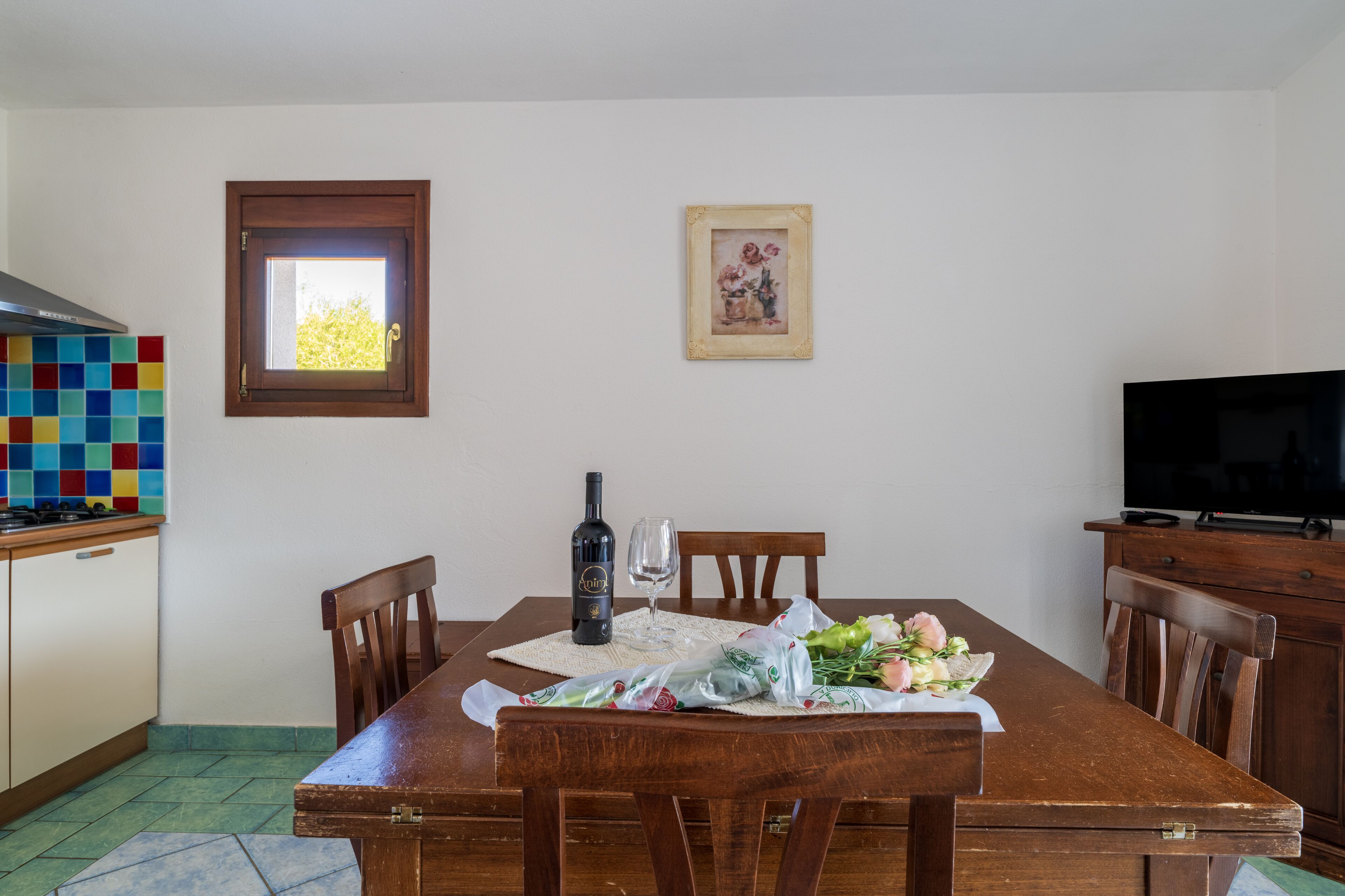 A dining area with a wooden table, chairs, a bottle of wine, and a bouquet of flowers.