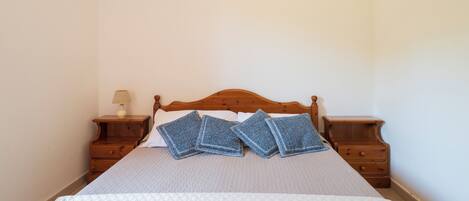 A neatly made bed with a wooden headboard, two bedside tables with lamps, and a plain wall.