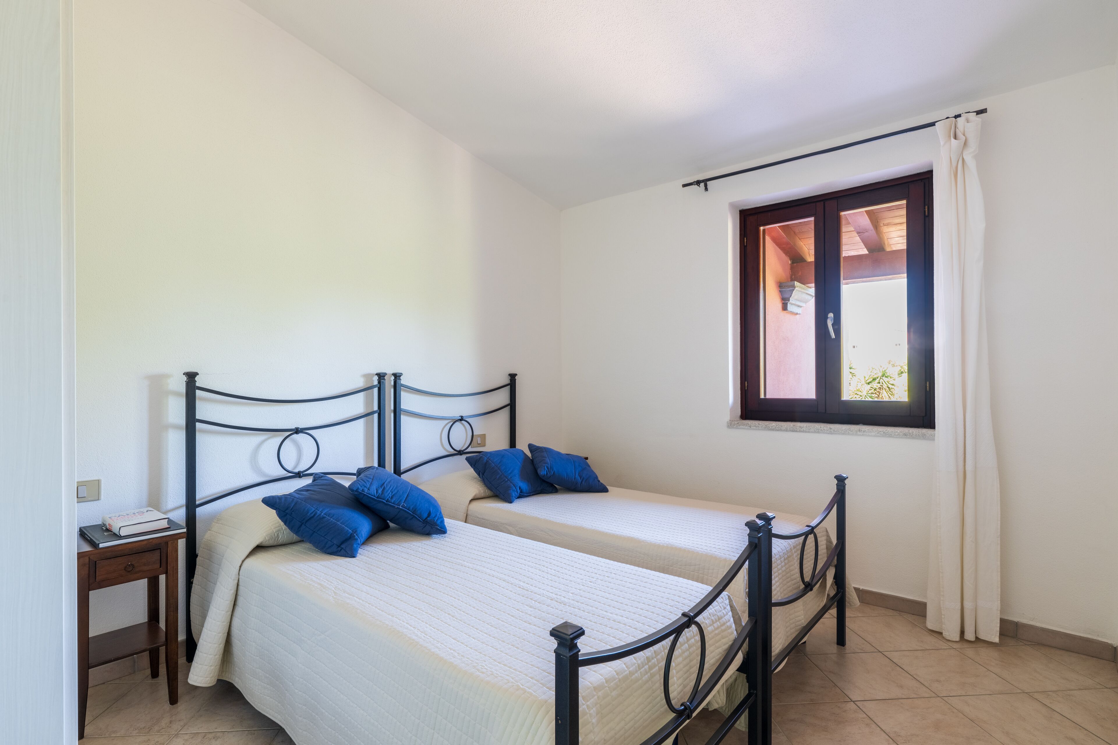 Une chambre avec deux lits simples, une table de chevet, une fenêtre avec des rideaux et une porte.
