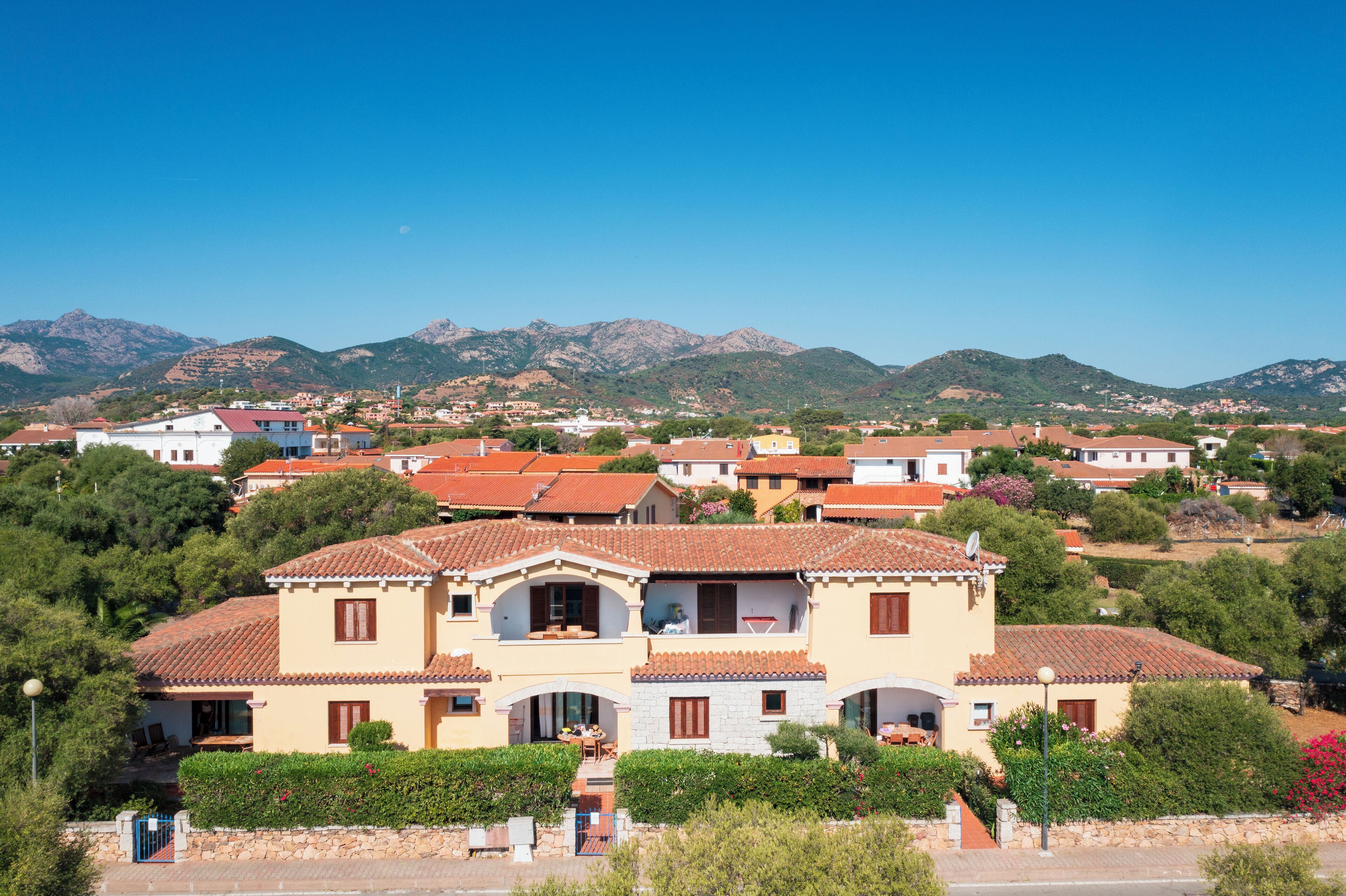 Une villa de style méditerranéen, avec un toit en tuiles, entourée d’une végétation luxuriante et avec des montagnes en toile de fond.