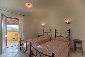 Two single beds with patterned bedspreads, a nightstand with a drawer, and a glass door leading to an outdoor area.