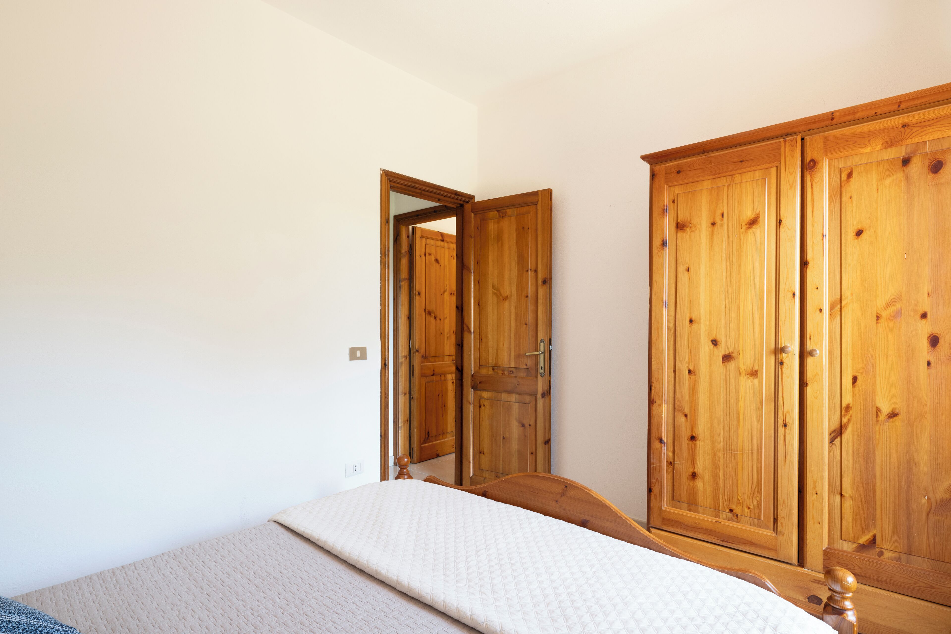 A bedroom with a bed, wooden wardrobe, and a door leading to another room.
