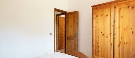 A bedroom with a bed, wooden wardrobe, and a door leading to another room.