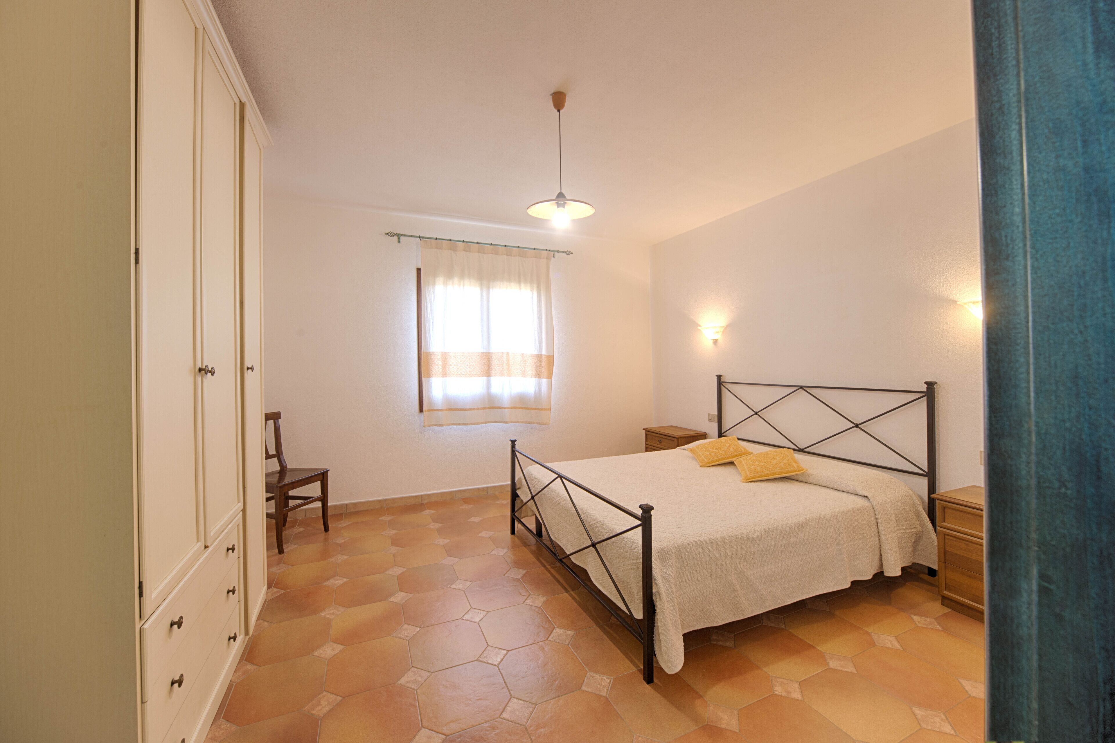 A bedroom with a bed, a wardrobe, a chair, and a window with curtains.