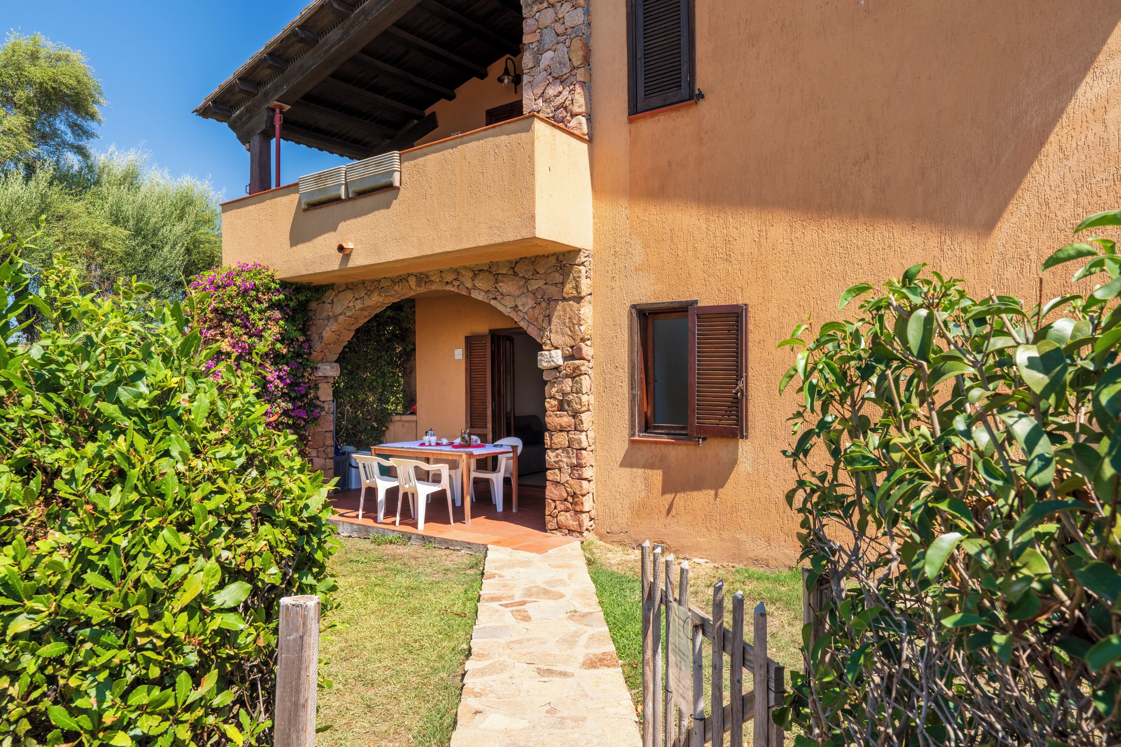 Una casa rústica con un arco de piedra, un balcón y una mesa con sillas afuera.