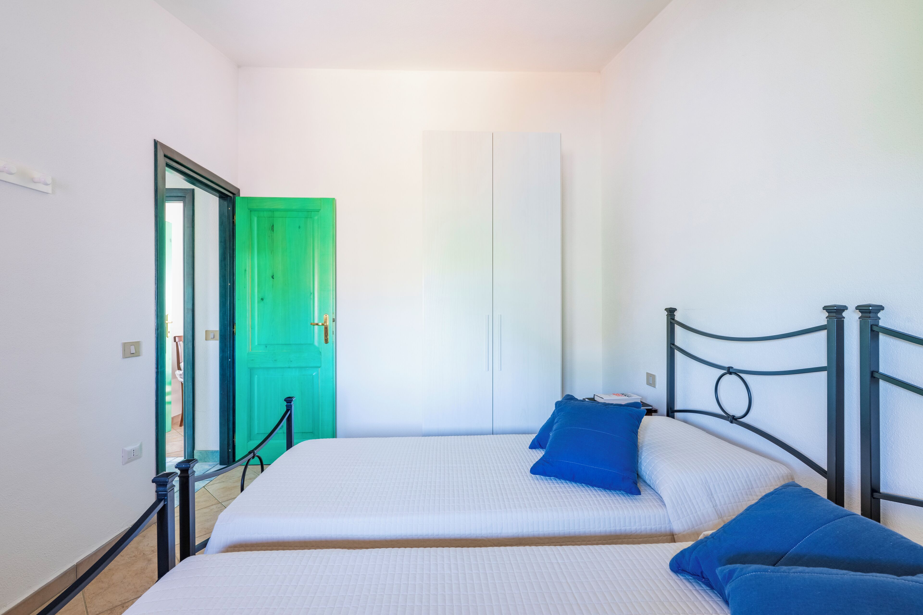 A small, clean room with a bed, a green door, and a white wardrobe.