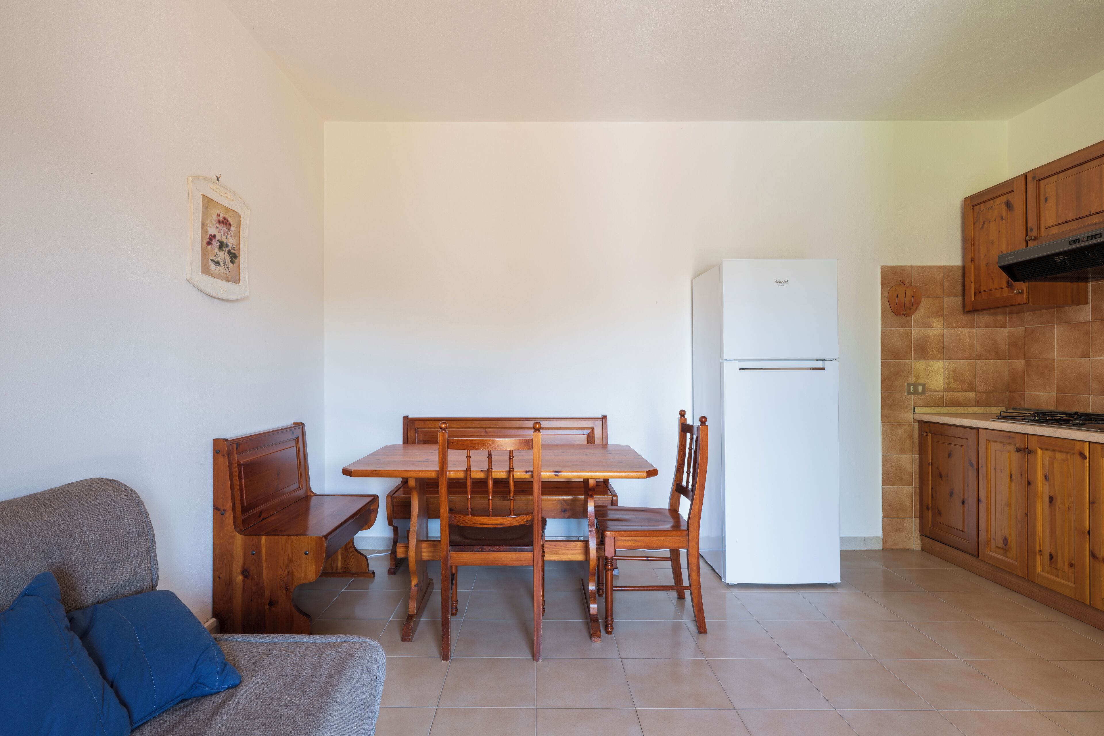 A compact kitchen with wooden cabinets, a white refrigerator, and a dining table with chairs.