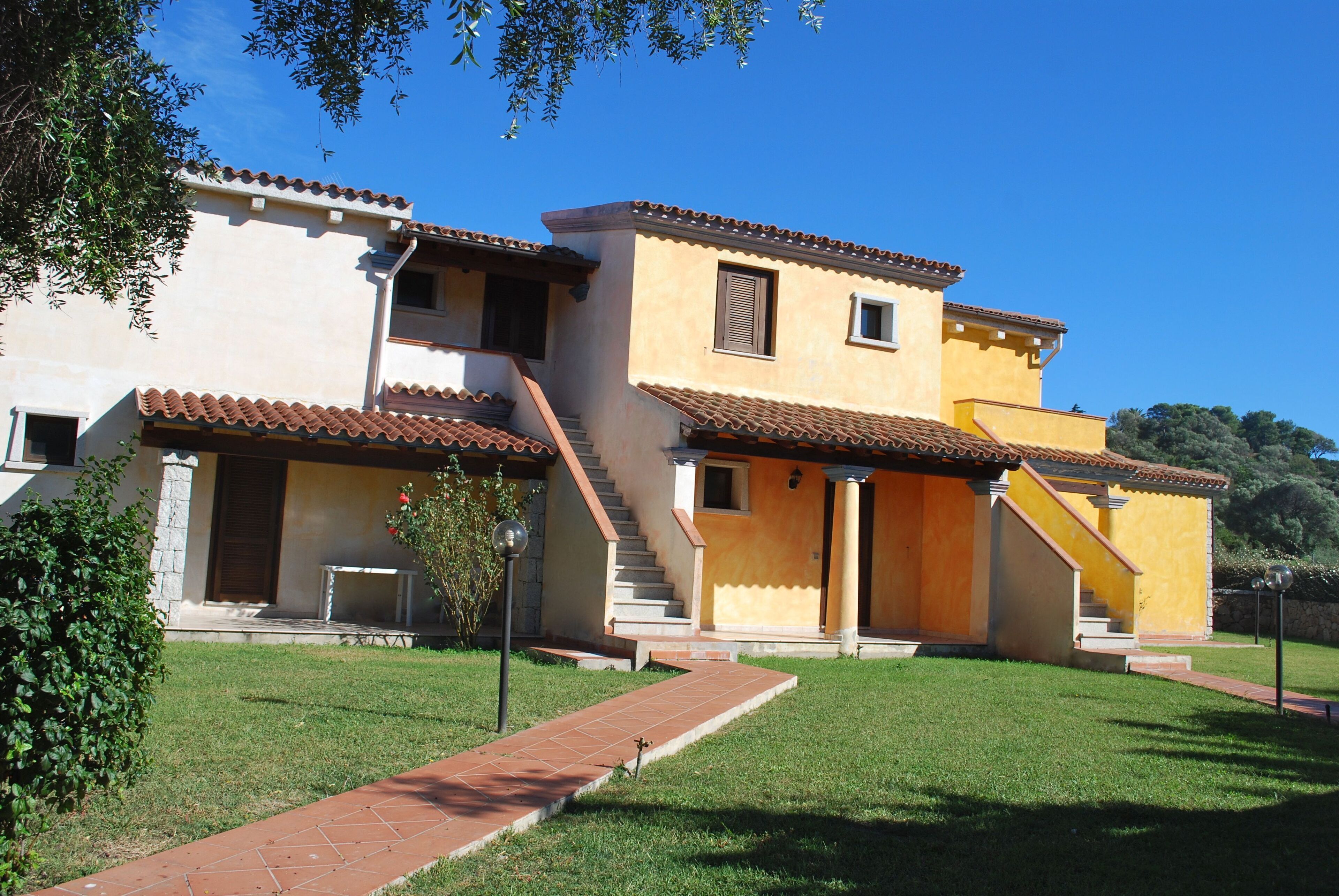 A two-story building with a tiled roof, a staircase, and a small garden area.