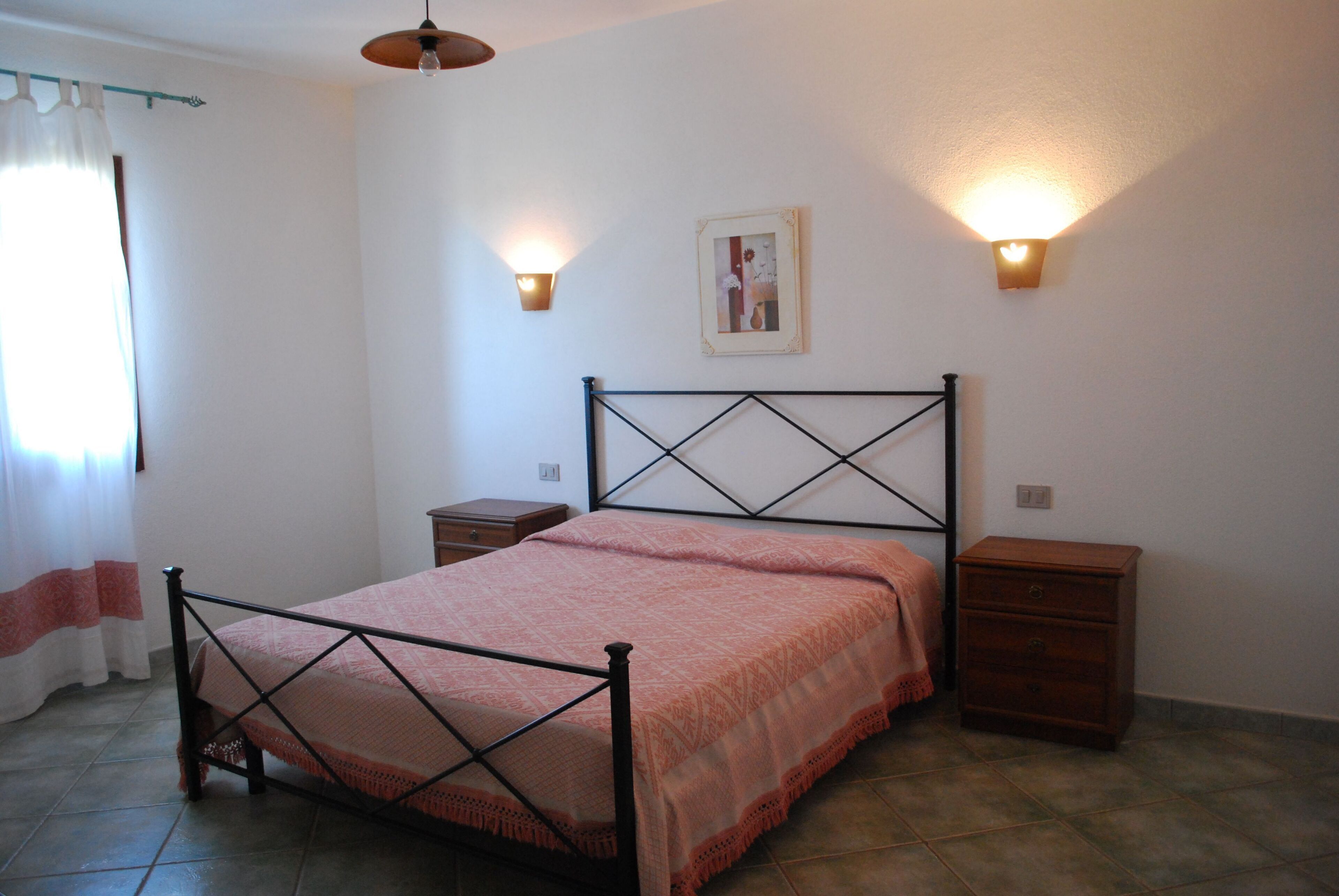 A bedroom with a bed, two nightstands, a wall-mounted light fixture, and a framed picture on the wall.
