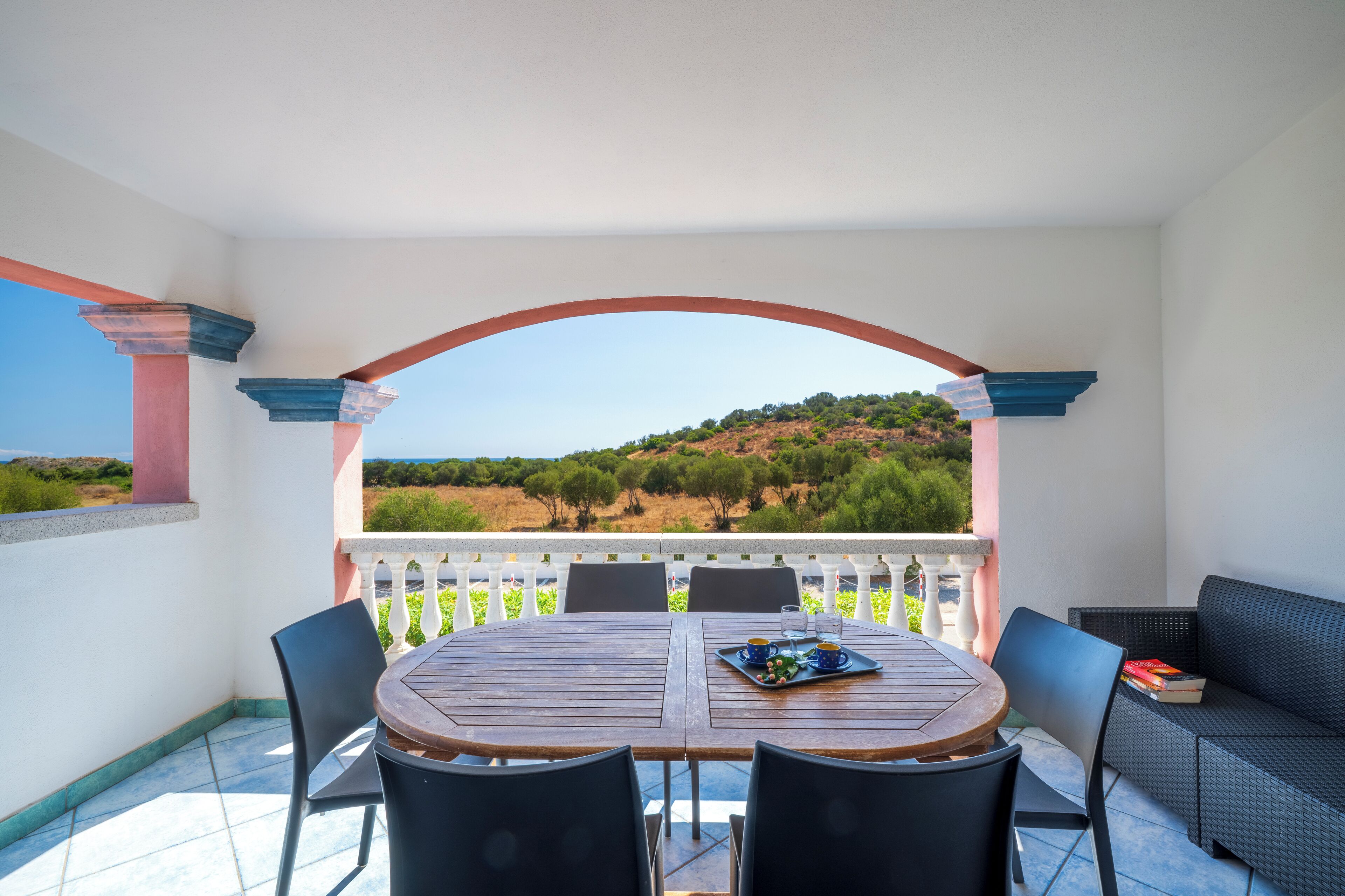 A terrace with a table and chairs, a sofa, and a view of a hilly landscape.