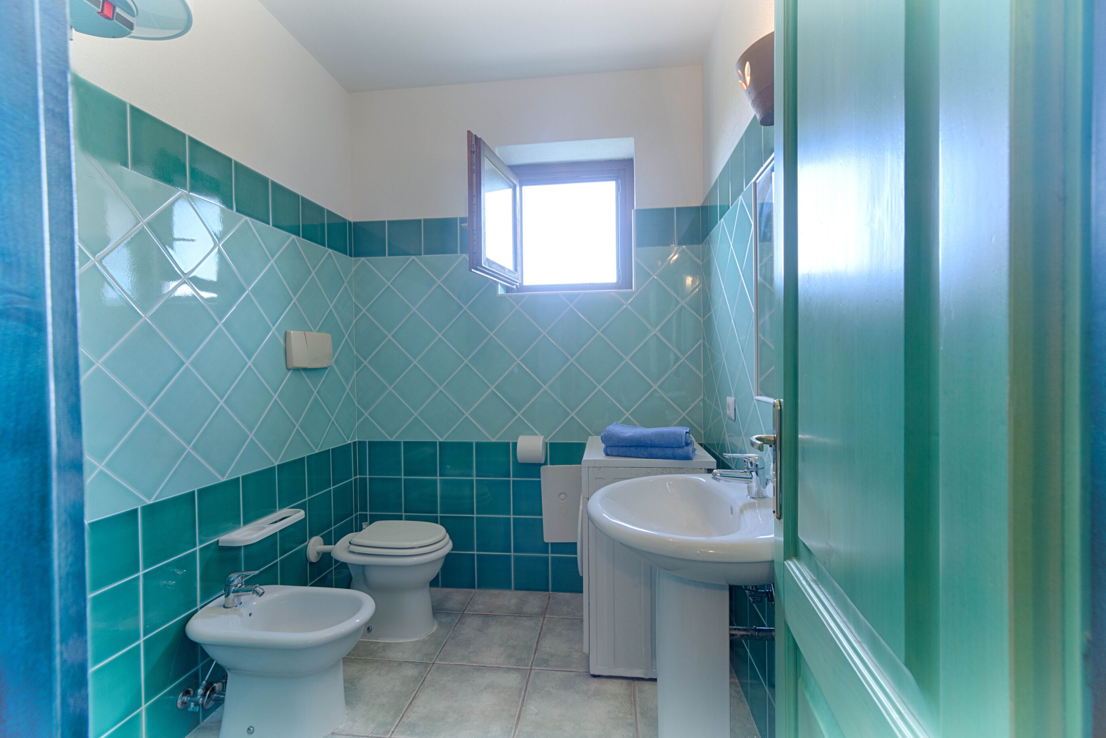 A bathroom with a toilet, bidet, and sink, tiled in a geometric pattern.