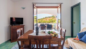 A dining area with a table set for two, a television on a cabinet, and a balcony with a view of the landscape. - Residence Oasi e Oasi Blu (San Teodoro)