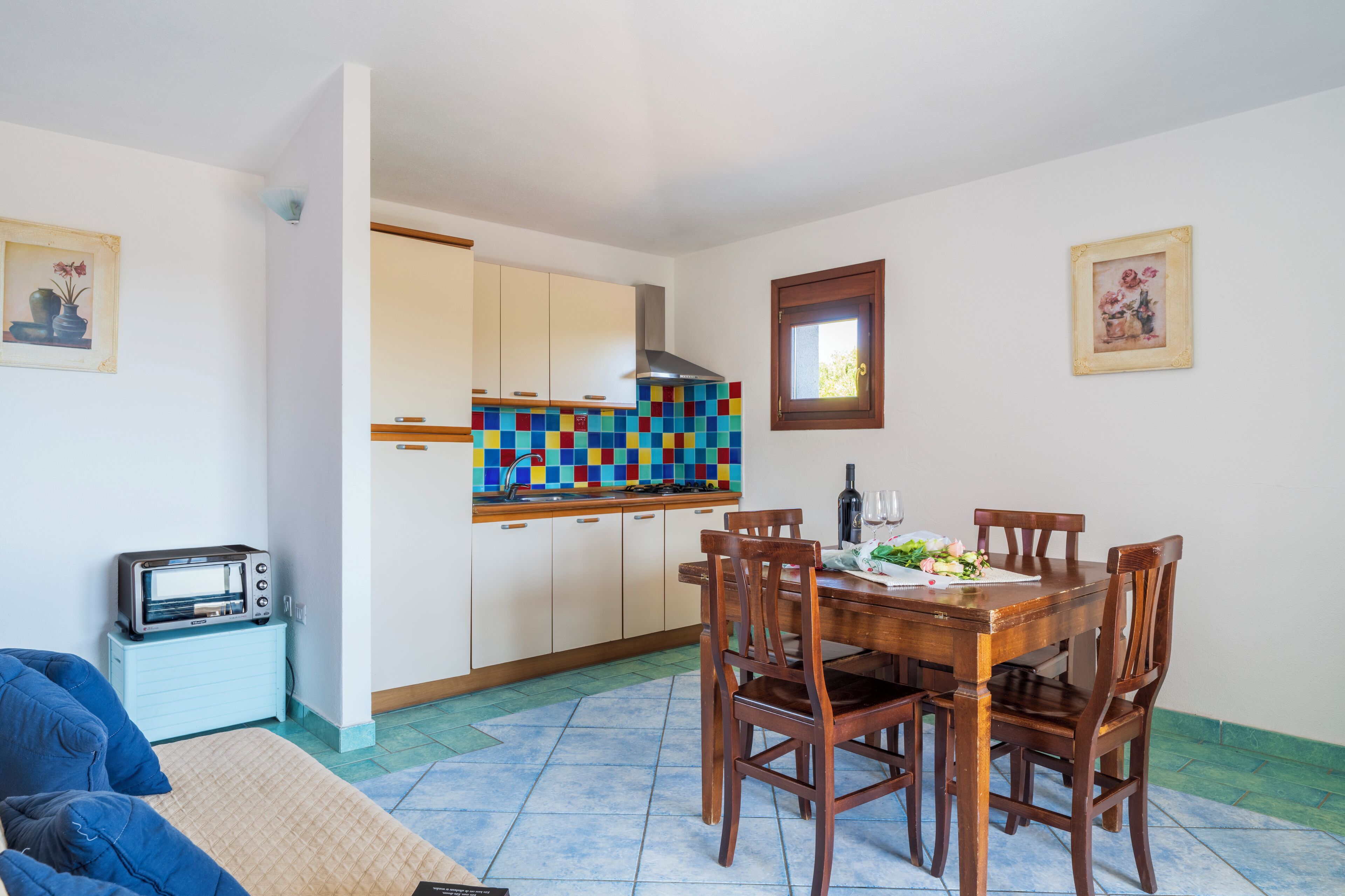 Una cocina compacta con salpicadero de azulejos, una mesa de comedor con sillas, horno empotrado y un refrigerador pequeño.