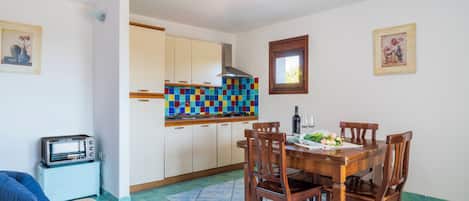 Una cocina compacta con salpicadero de azulejos, una mesa de comedor con sillas, horno empotrado y un refrigerador pequeño.
