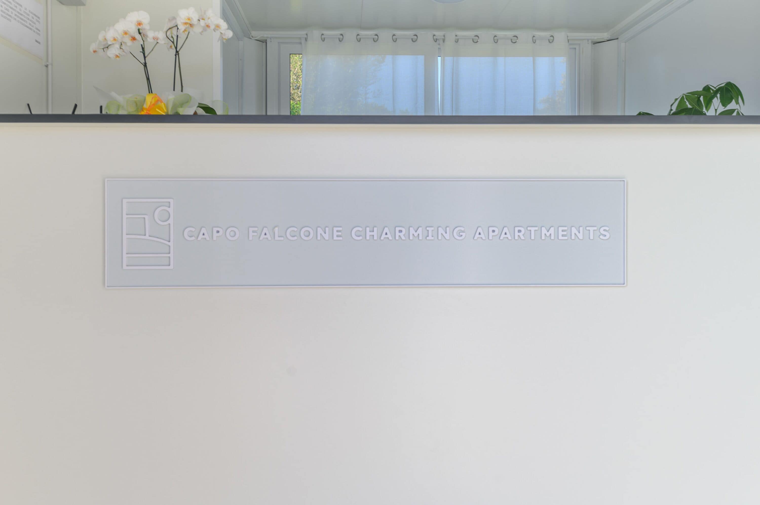 Un espace d’accueil avec une enseigne indiquant « Capo Falcone Charming Apartments ».