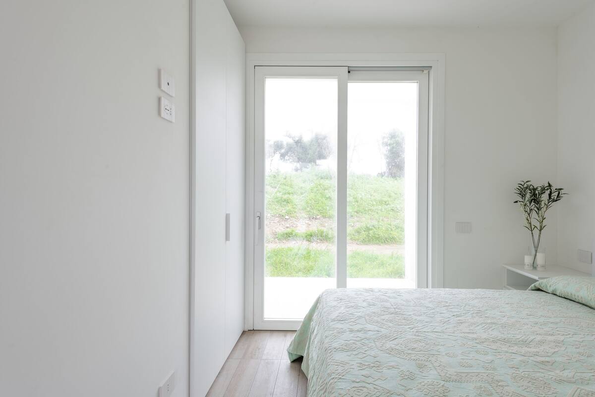 A bedroom with a bed, a nightstand, a window with a view of greenery, and a sliding door.