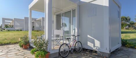 Ein modernes, weißes Gebäude mit einem Geschoss, mit überdachter Terrasse, einem Fahrrad und Blumentöpfen.