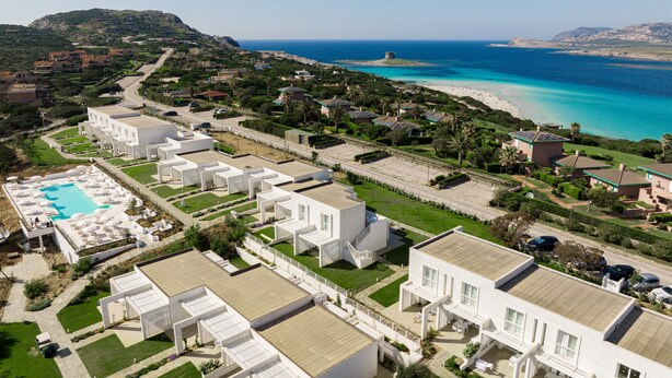 Un complejo turístico costero con varias edificaciones blancas, una piscina y una playa.