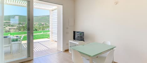 Une chambre moderne dotée d’une porte-fenêtre coulissante donnant sur un espace extérieur, d’une table en verre avec des chaises et d’un téléviseur posé sur un meuble.