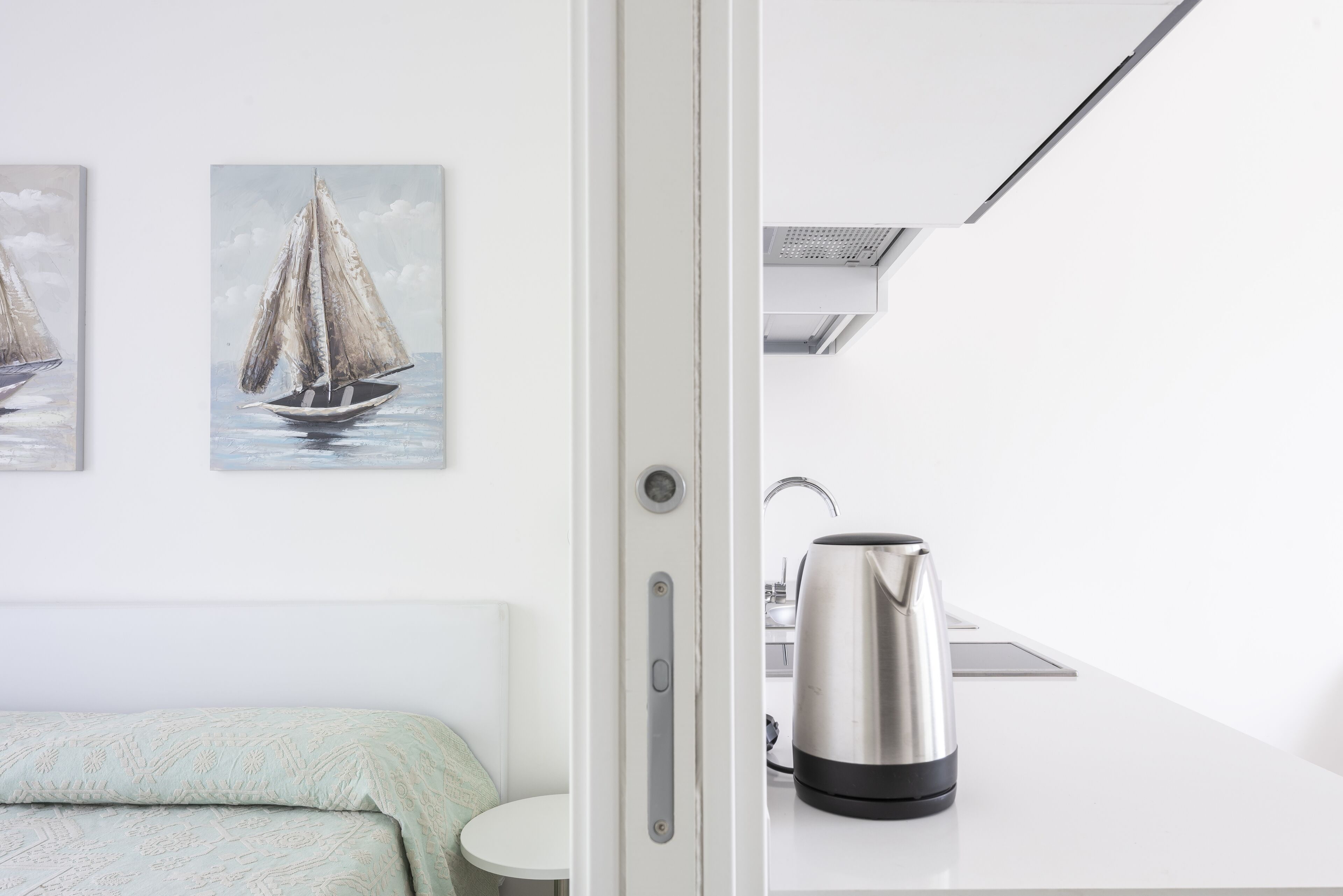Camera d'albergo moderna con un letto, un tavolino rotondo, un bollitore e due dipinti raffiguranti vele.