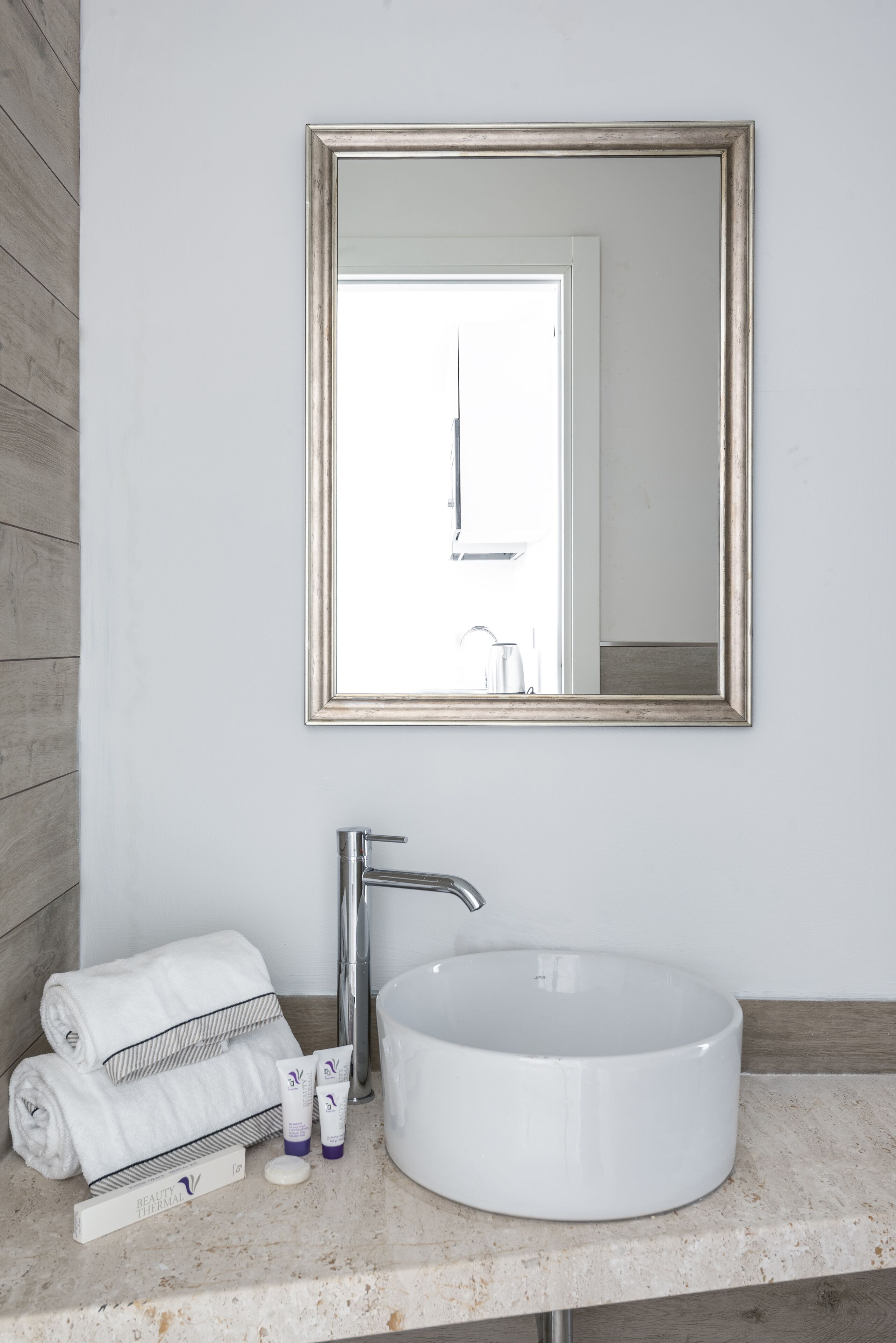 A bathroom with a white sink, a large mirror, and a towel rack with folded towels.