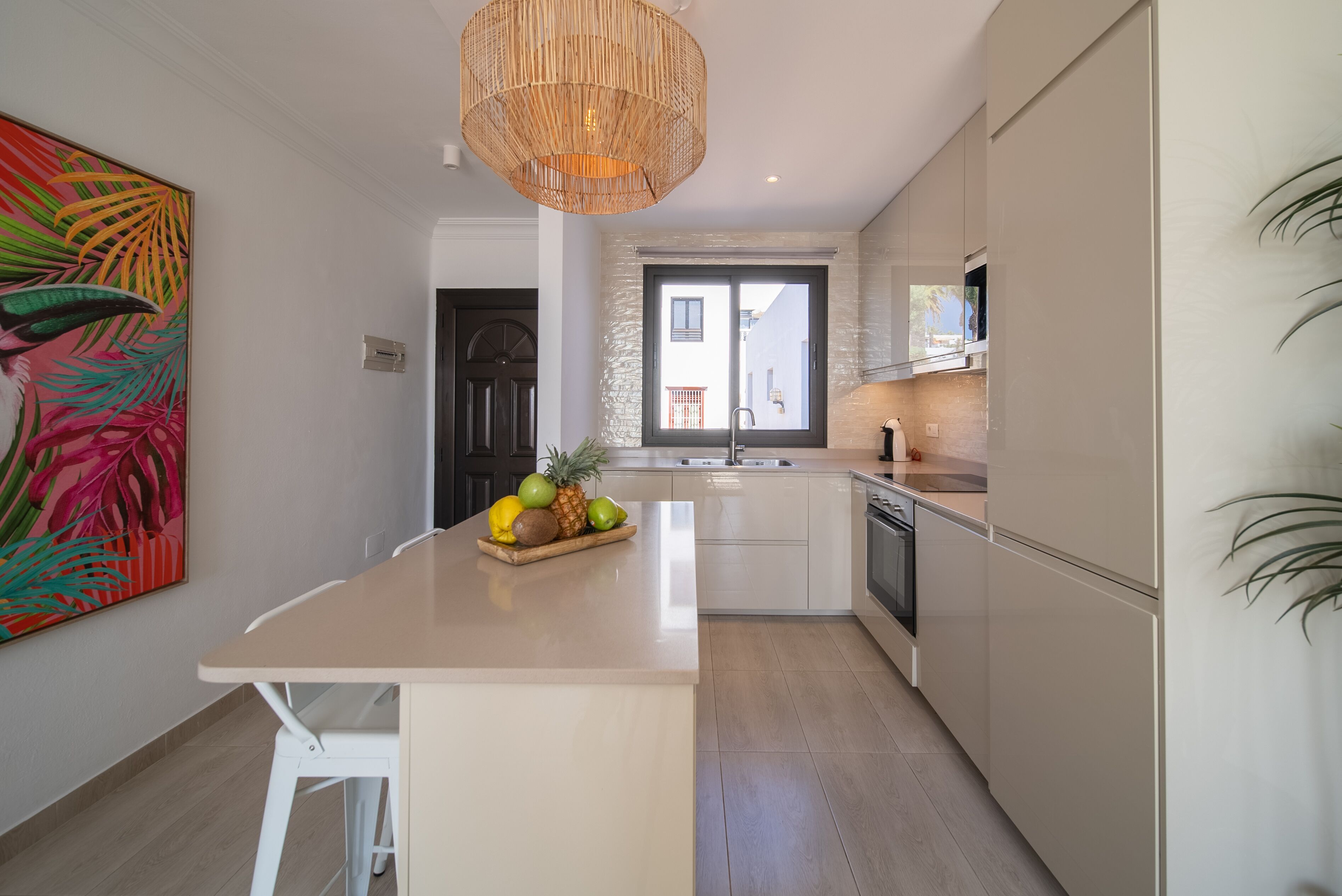 Una cocina moderna con una isla central, armarios blancos y un ventanal grande.