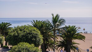 Een strand met palmbomen, een heldere lucht en een vliegtuig in de verte.