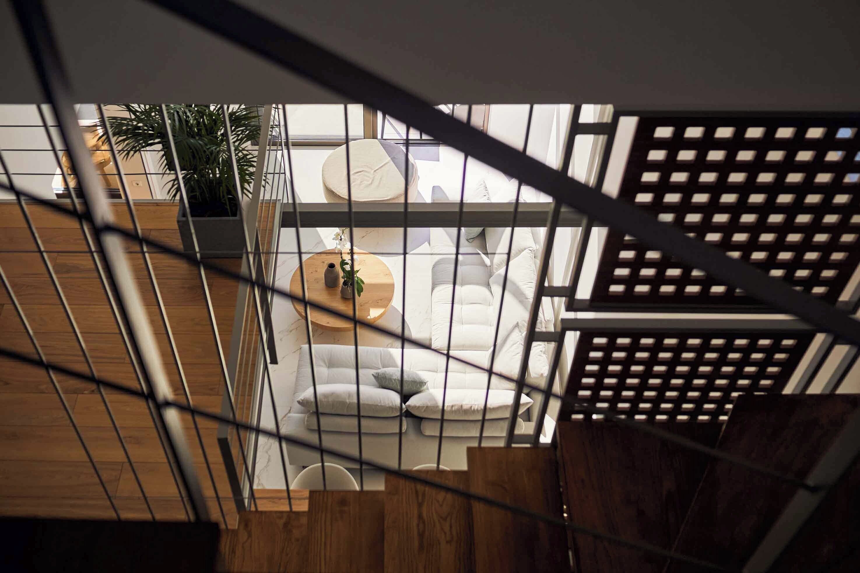 Un interior moderno con una escalera de madera, un conjunto de sofá blanco y una planta en maceta.