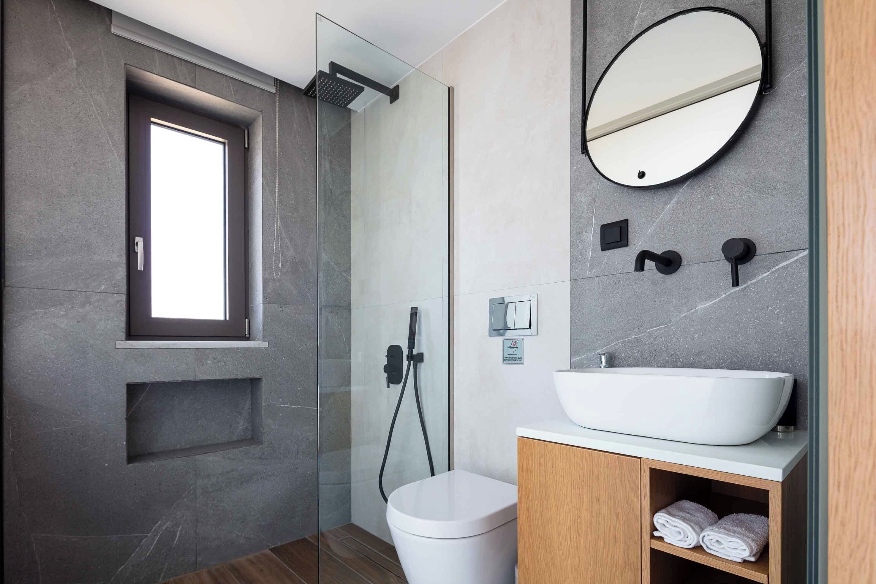 Un baño moderno con ducha envuelta en vidrio, lavamanos blanco y tocador de madera.