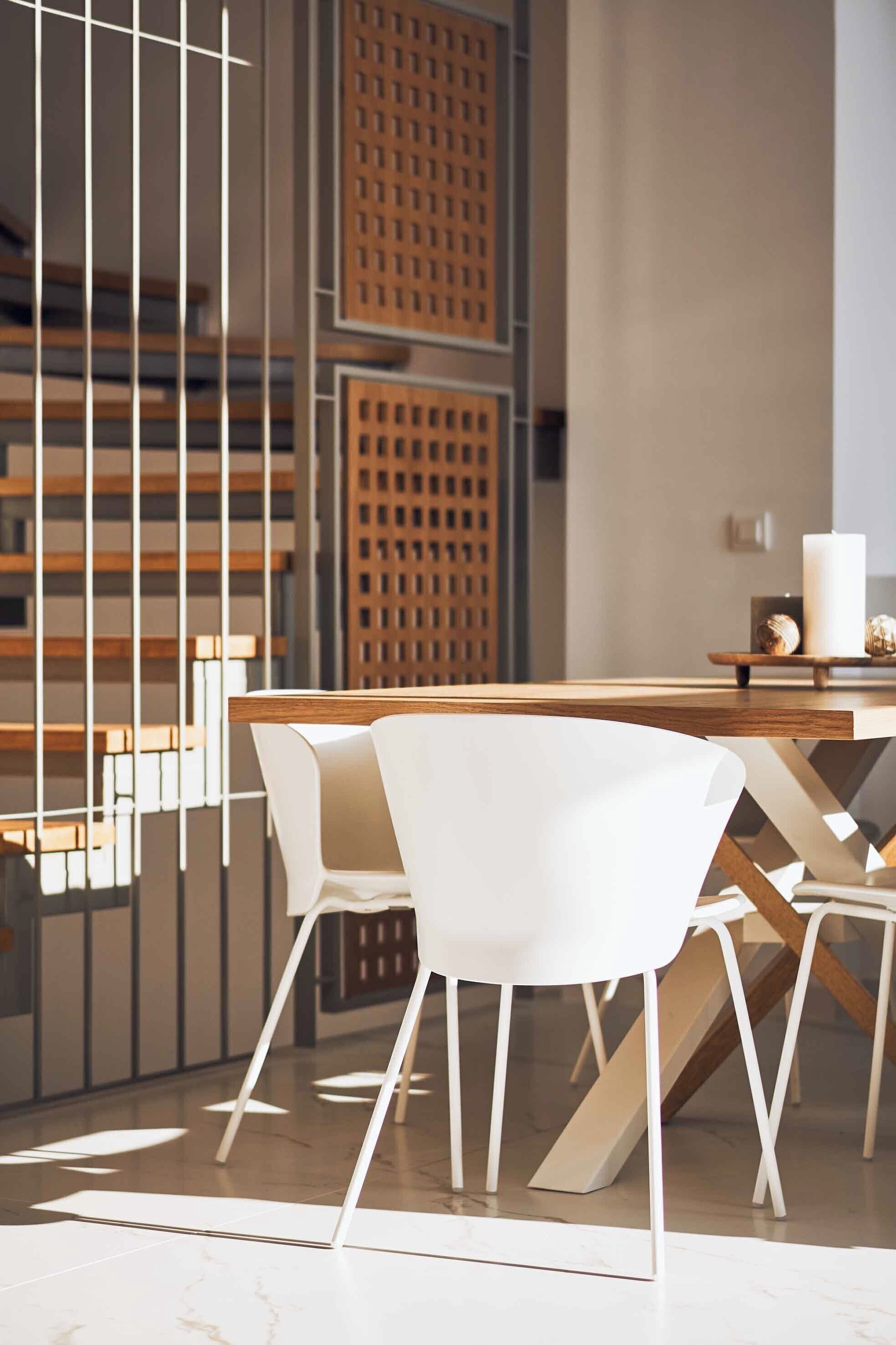 Uma área de refeições moderna com uma mesa de madeira e cadeiras brancas, uma parede decorativa com padrões geométricos e uma vela branca grande sobre a mesa.