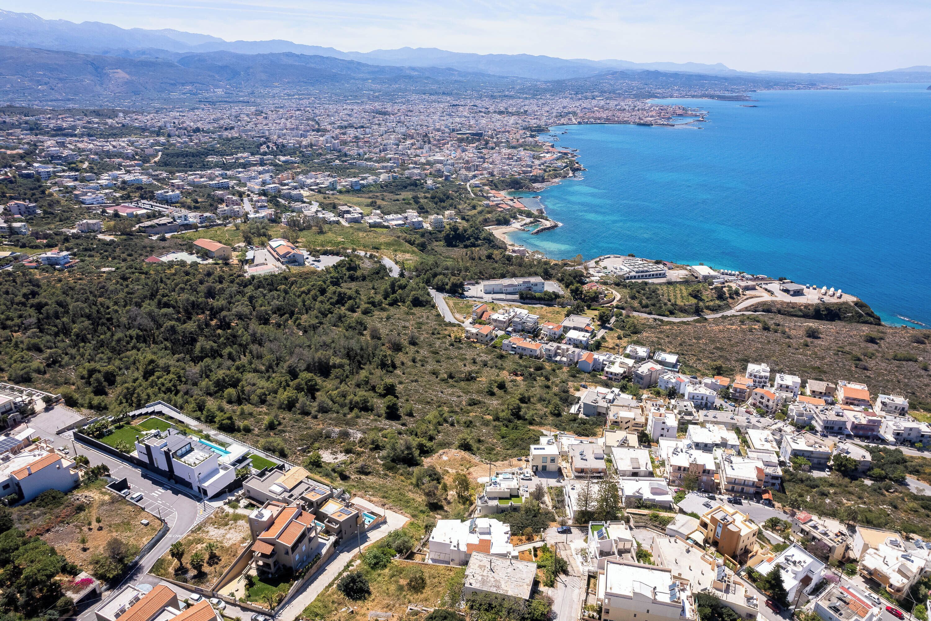 An aerial view of a coastal town with residential buildings, a marina, and a mountainous backdrop.