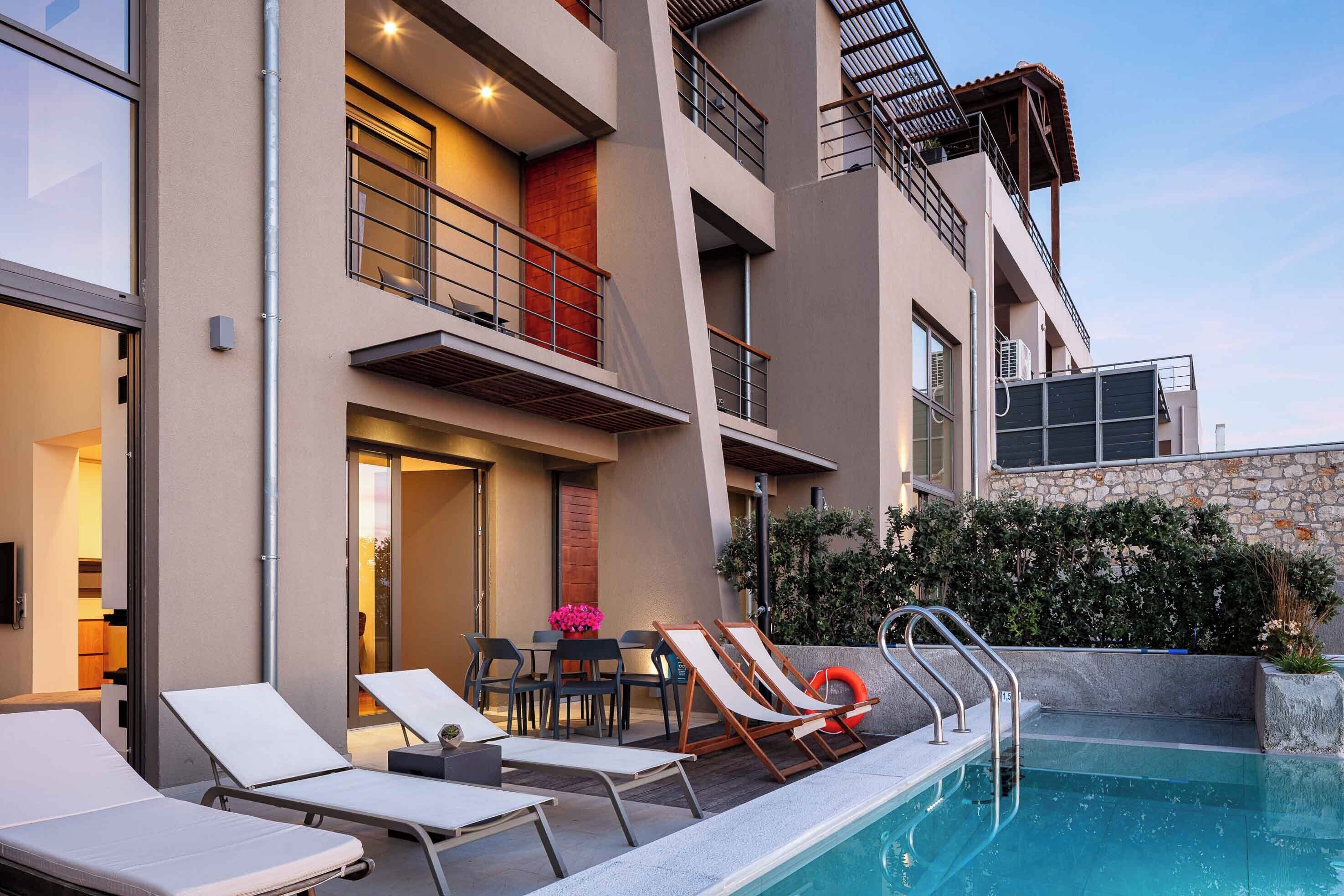 A modern building with a pool area, including lounge chairs and a table with flowers.